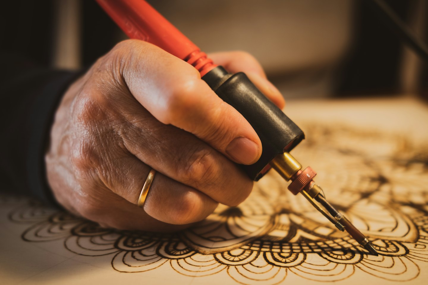 Hand benutzt Pyrographie-Werkzeug, um Muster auf Holz zu brennen.