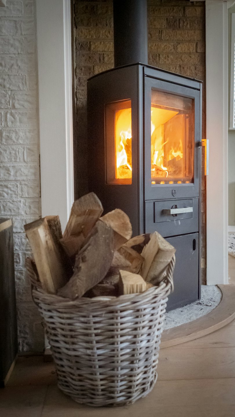 Holzofen mit hellem Feuer und Holzkorb.