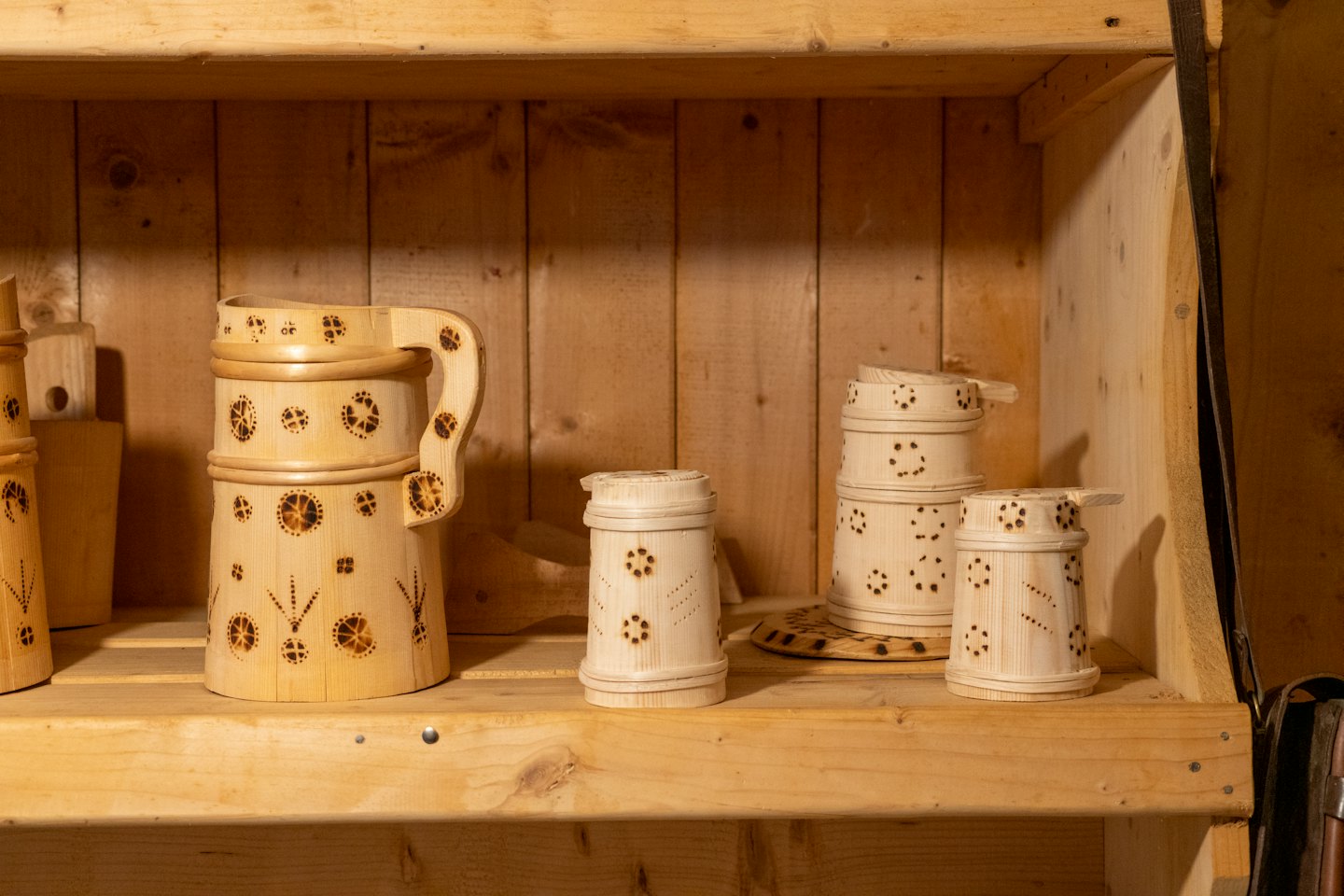 Handgefertigte Holzbecher mit dekorativen Mustern stehen in Holzregalen.