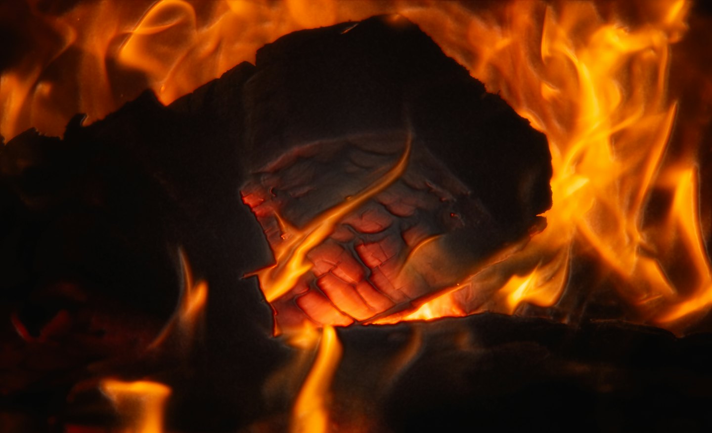 Ein Stück Holz brennt mit hellorangen Flammen.