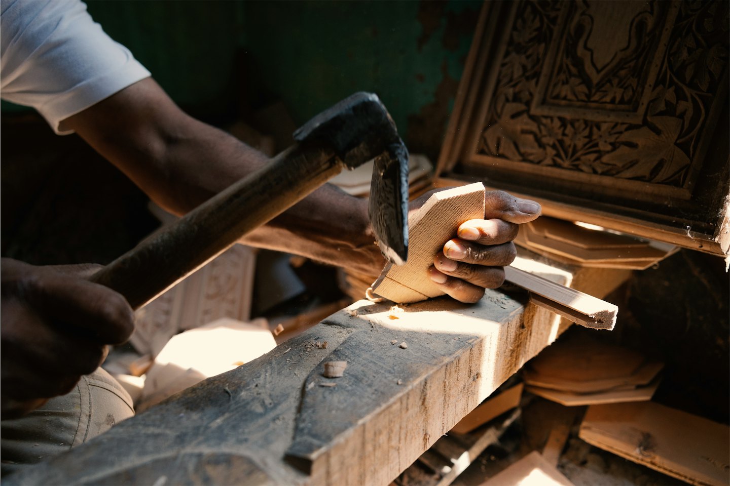 Handwerker schnitzt filigrane Details in helles Holz mit einem Werkzeug.