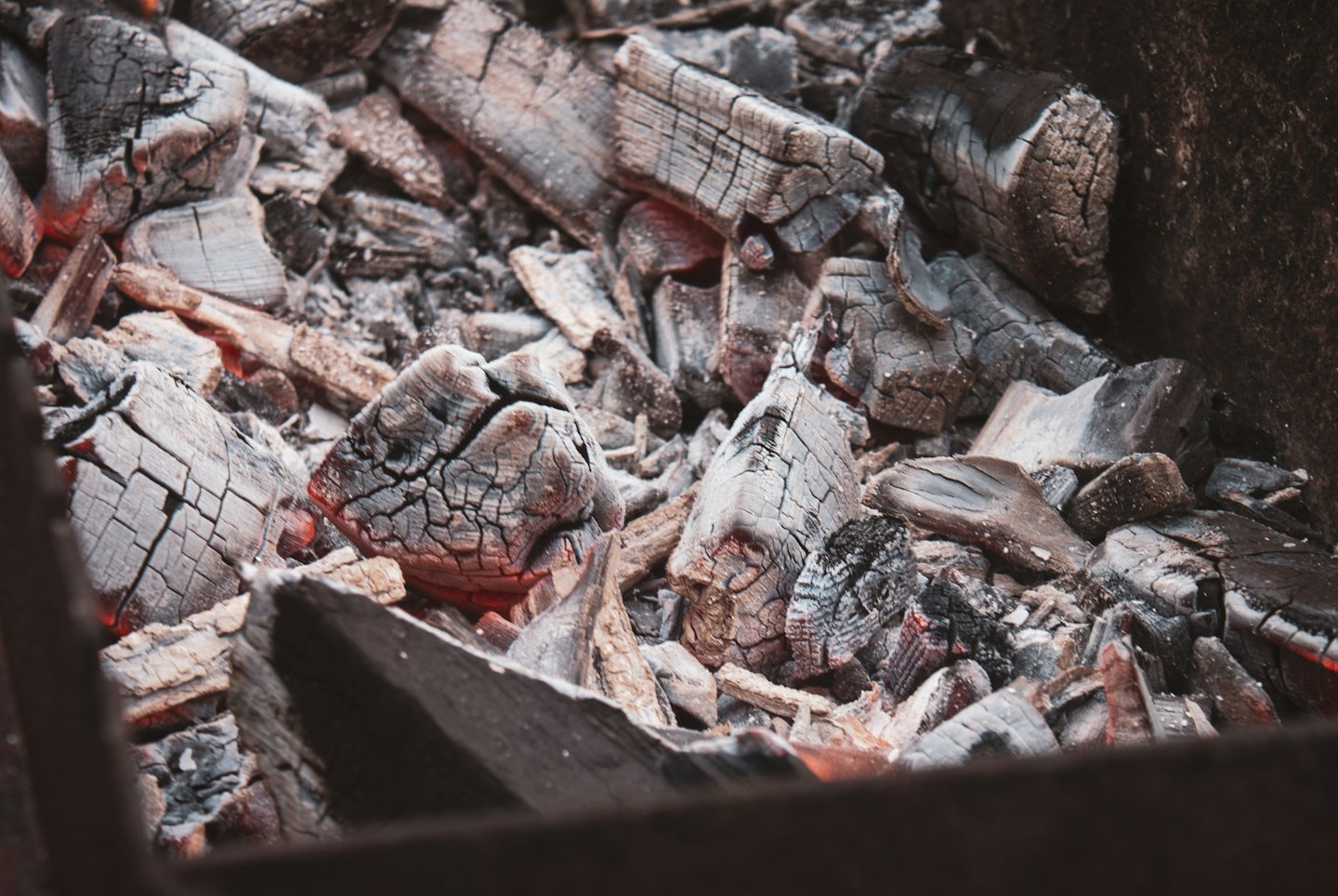 Glühende Kohlen schwelen zwischen verkohlten Holzstücken und Asche.